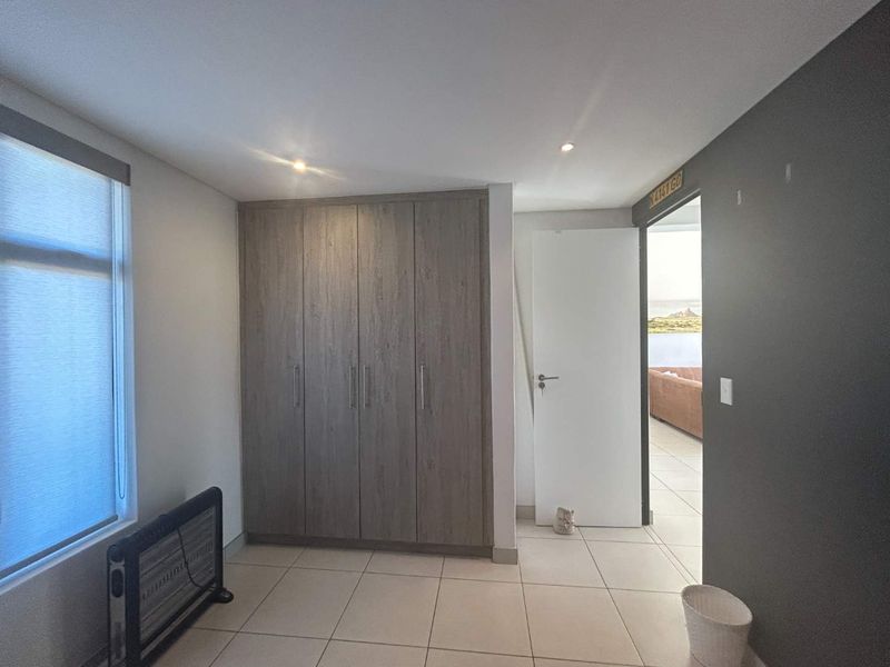 A clean, empty bedroom featuring neutral tiled flooring, recessed downlighting, and modern wood-finish built-in cupboards.