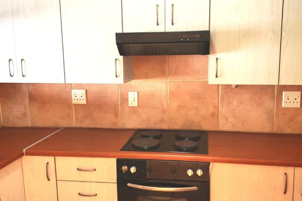 A functional kitchen featuring light wood-finish cabinetry, a dark laminate countertop, built-in oven, electric hob, and tiled backsplash.