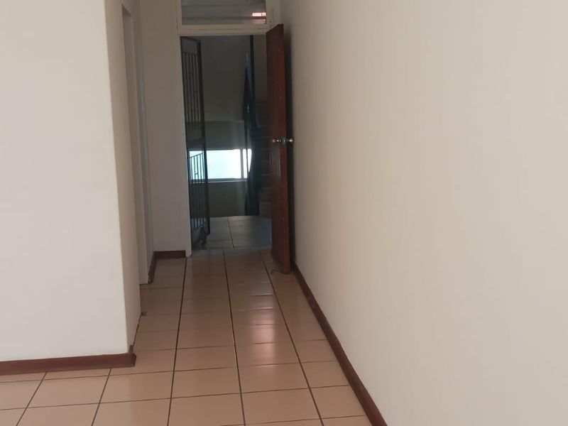 A simple, empty hallway featuring neutral ceramic floor tiles and white walls, leading towards an entrance door.