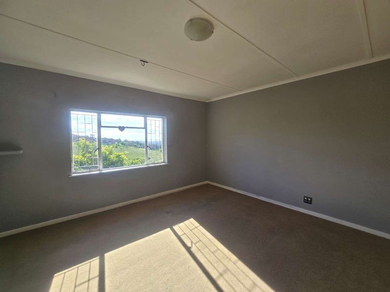 An empty bedroom featuring grey walls, carpet flooring, and a window with security bars offering a scenic view.