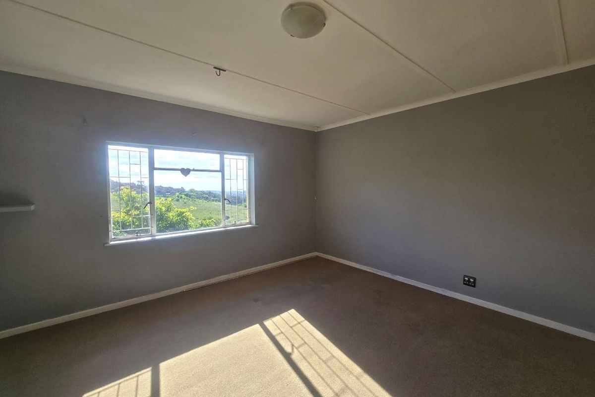 An empty bedroom featuring grey walls, carpet flooring, and a window with security bars offering a scenic view.
