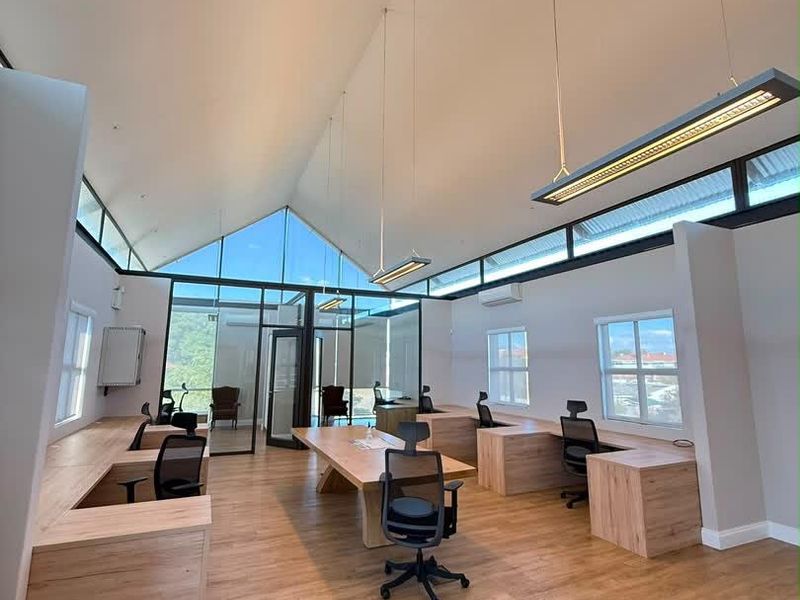 Modern open-plan office space featuring high vaulted ceilings, clerestory windows, integrated wooden workstations, and contemporary suspended lighting fixtures.