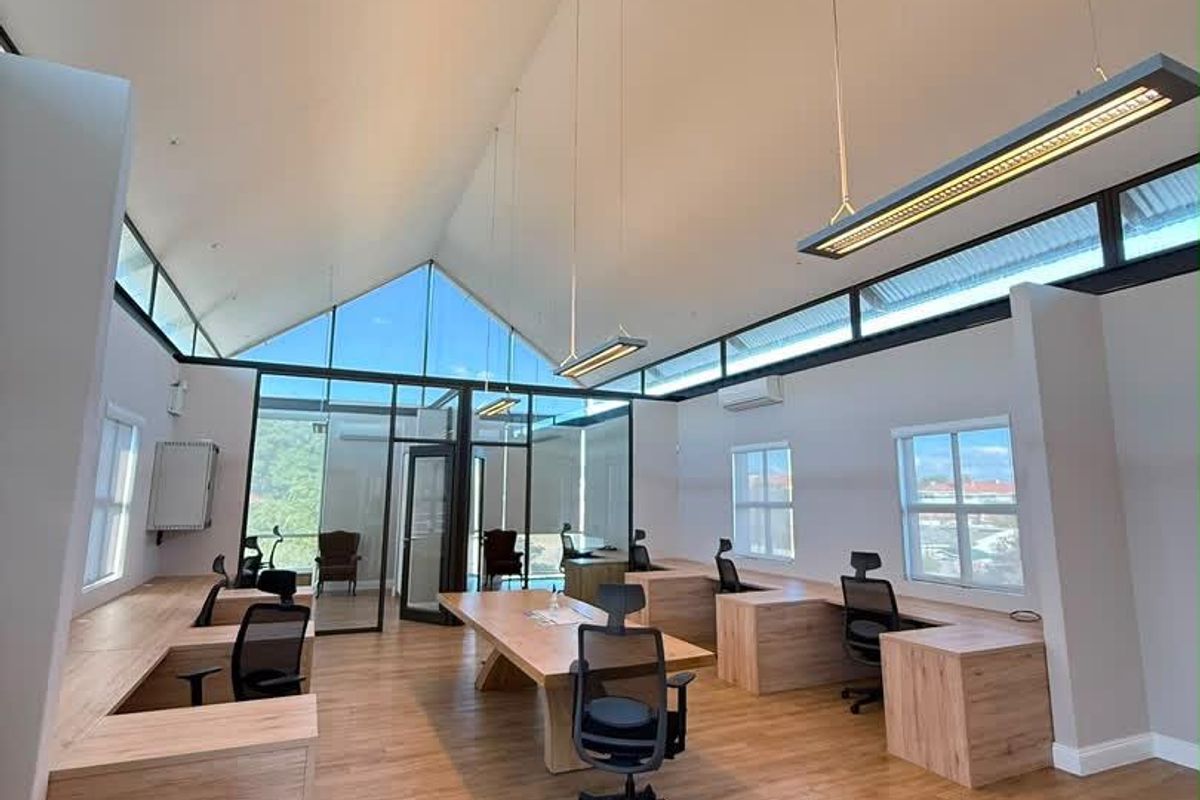 Modern open-plan office space featuring high vaulted ceilings, clerestory windows, integrated wooden workstations, and contemporary suspended lighting fixtures.