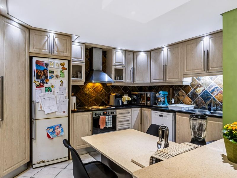 A functional kitchen featuring wood-finish cabinetry, stone countertops, a central island, and a tiled backsplash with integrated oven and extractor fan.