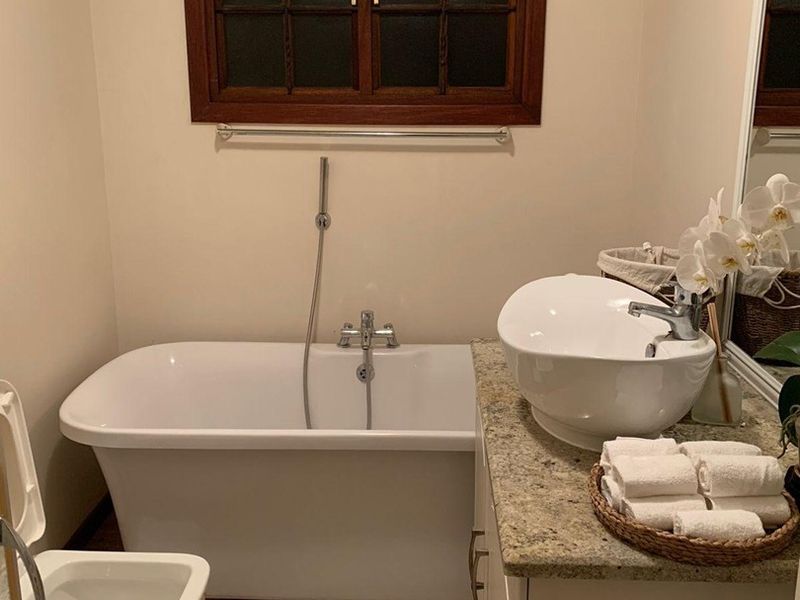 A well-maintained bathroom featuring a freestanding bathtub, vessel sink on a granite vanity, and a timber-framed window.