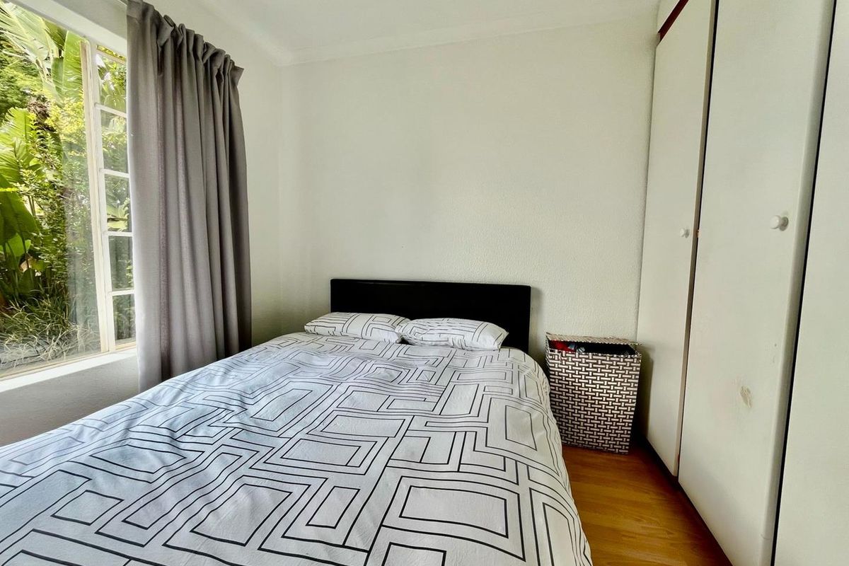 A bedroom featuring built-in wardrobes, laminate flooring, and a window with garden views.