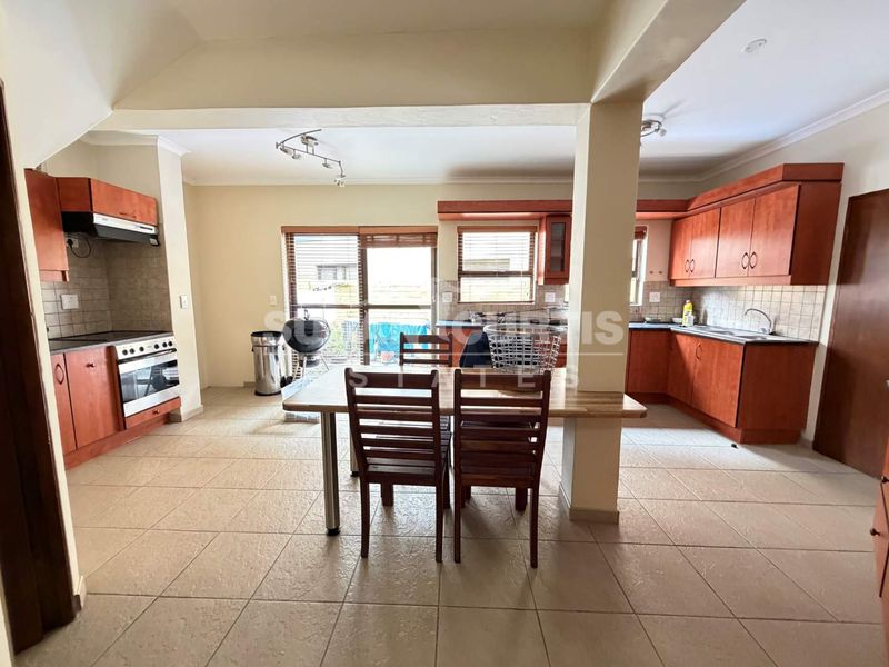 Open plan kitchen and dining area featuring wooden cabinetry, tiled flooring, and direct access to the outdoor patio through sliding glass doors.