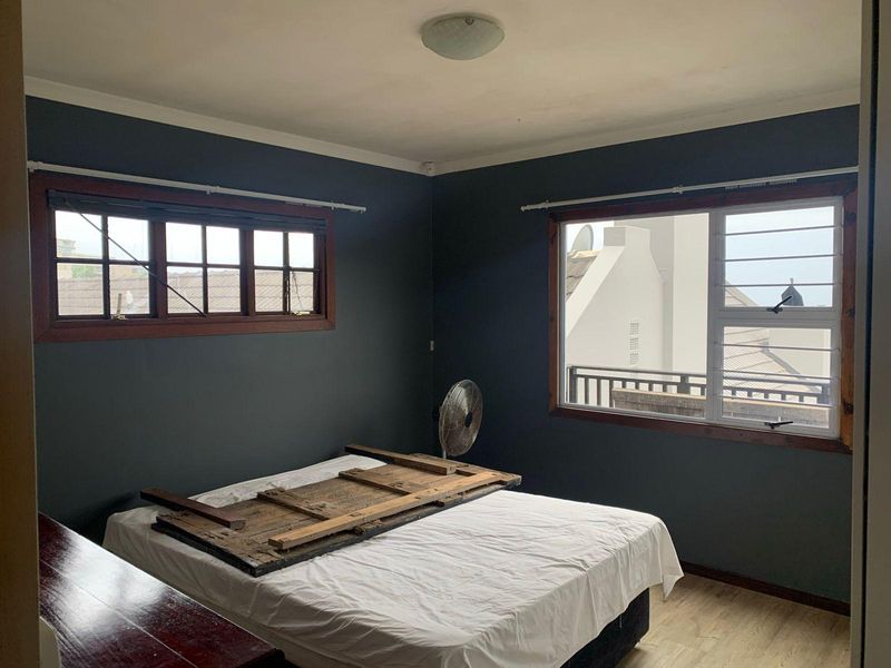 A bedroom featuring dark painted walls, laminate flooring, and timber-framed windows with security bars, offering a blank canvas for interior design updates.
