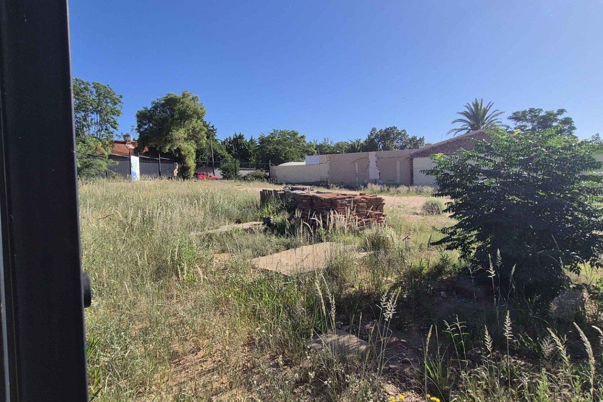 A view of a vacant residential plot featuring overgrown grass, a concrete slab, and perimeter fencing, suitable for future development.