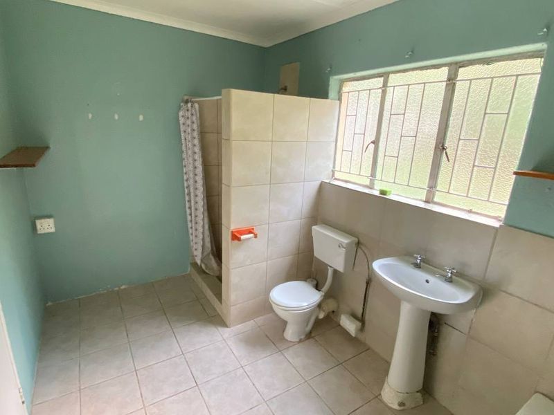 A functional bathroom featuring a pedestal basin, toilet, and a tiled shower enclosure with natural light from a window with security bars.