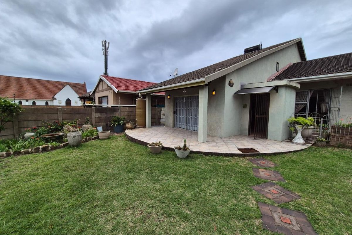 Rear view of the townhouse featuring a tiled patio, landscaped garden, paved walkway, and secure boundary walling.