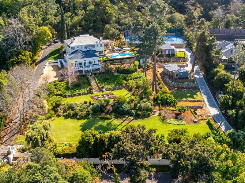 Aerial view of a large residential property featuring a multi-level house, swimming pool, tennis court, and extensive landscaped gardens.
