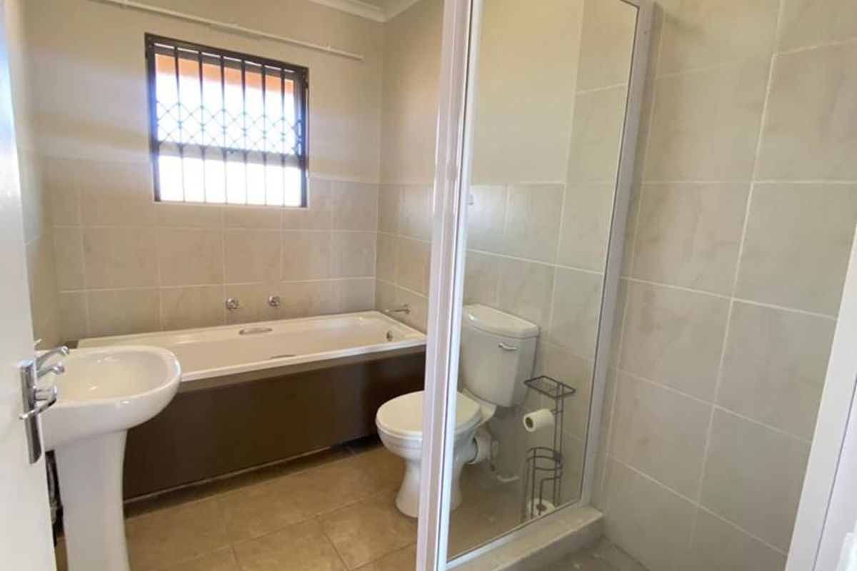 A functional bathroom featuring a pedestal basin, bathtub, separate shower enclosure with a rain shower head, and tiled finishes throughout.