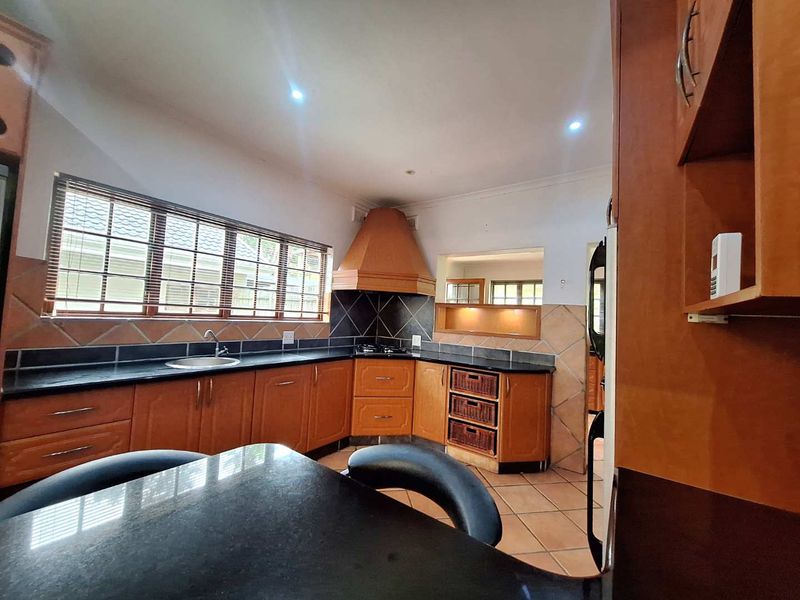 A functional kitchen featuring wooden cabinetry, granite countertops, a built-in hob with extractor fan, and tiled flooring with ample natural light.