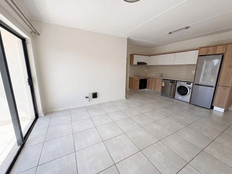 Modern open-plan living area featuring tiled floors, a sleek kitchen with built-in cabinetry, and a sliding door leading to an outdoor space.