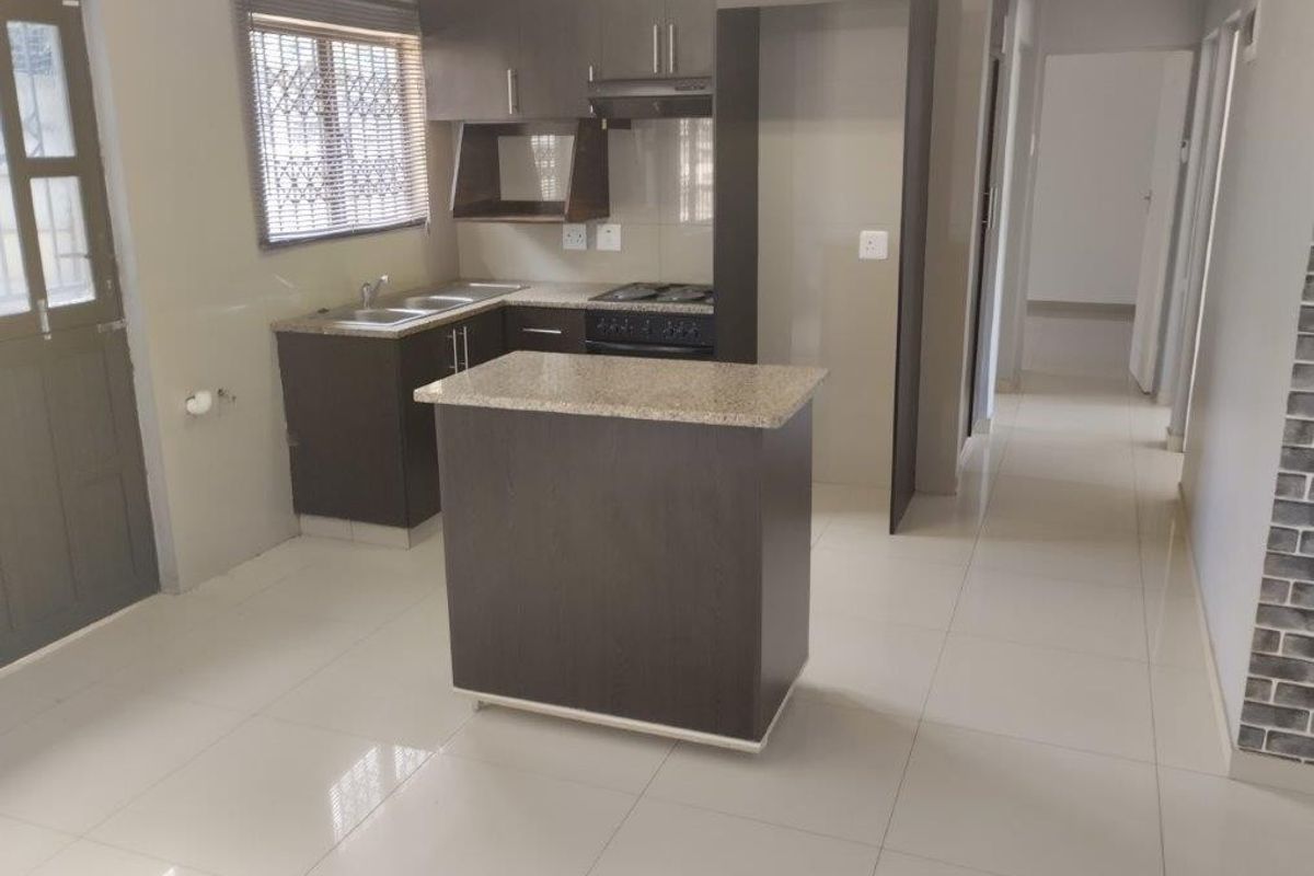 A clean, modern kitchen featuring dark cabinetry, granite countertops, a central island, and built-in cooking appliances with tiled flooring throughout.
