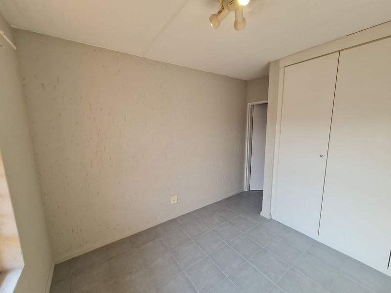 An empty bedroom featuring tiled flooring, a built-in wardrobe, and a ceiling-mounted light fixture, requiring minor cosmetic updates to the wall finishes.