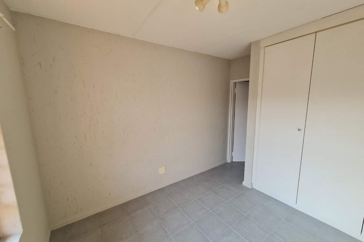 An empty bedroom featuring tiled flooring, a built-in wardrobe, and a ceiling-mounted light fixture, requiring minor cosmetic updates to the wall finishes.