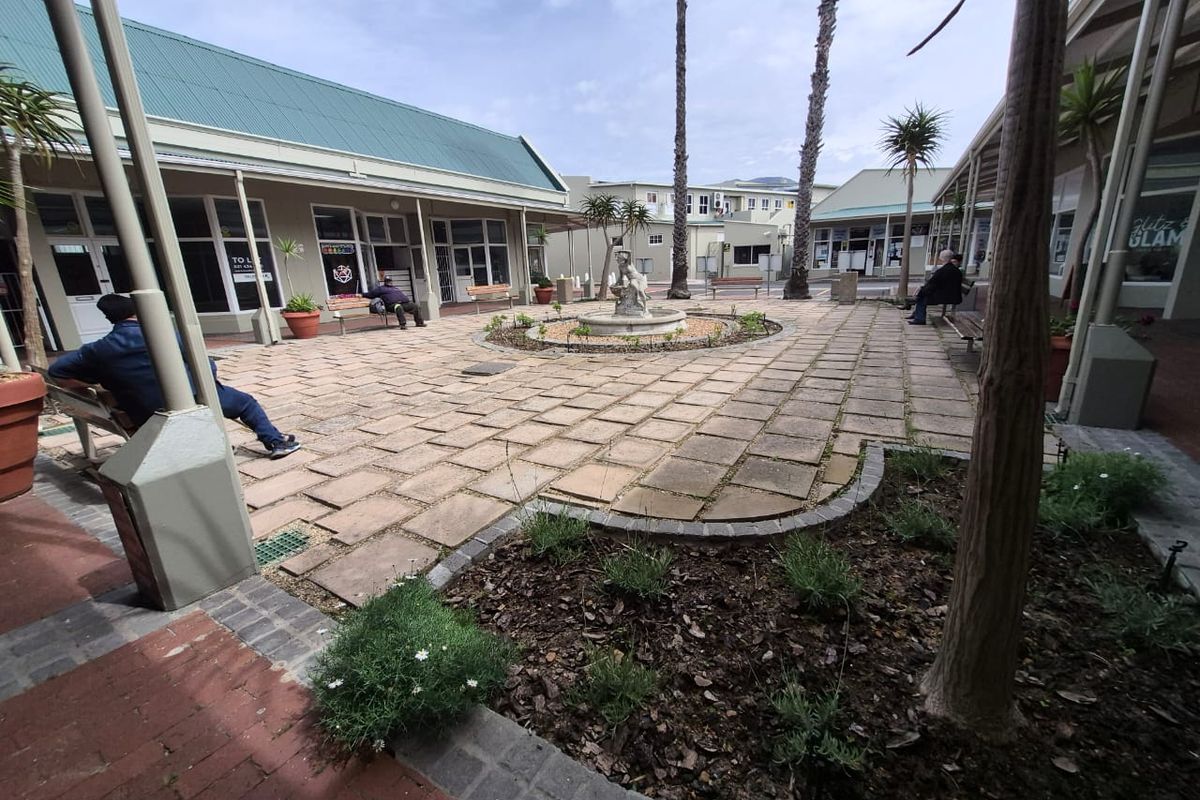A well-maintained retail courtyard featuring paved walkways, a central water fountain, and covered access to surrounding commercial units.