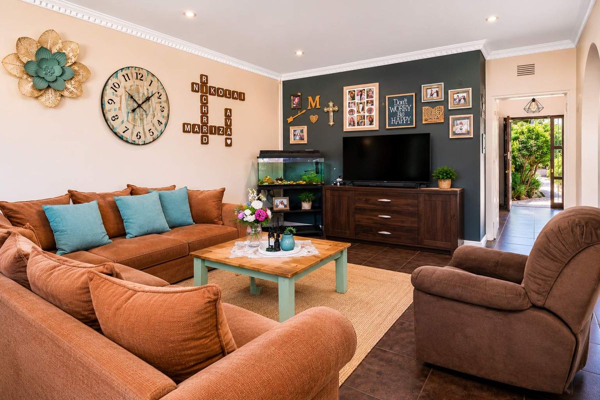 A well-maintained living room featuring tiled flooring, recessed downlighting, and decorative crown molding, with a direct view through to the rear garden area.