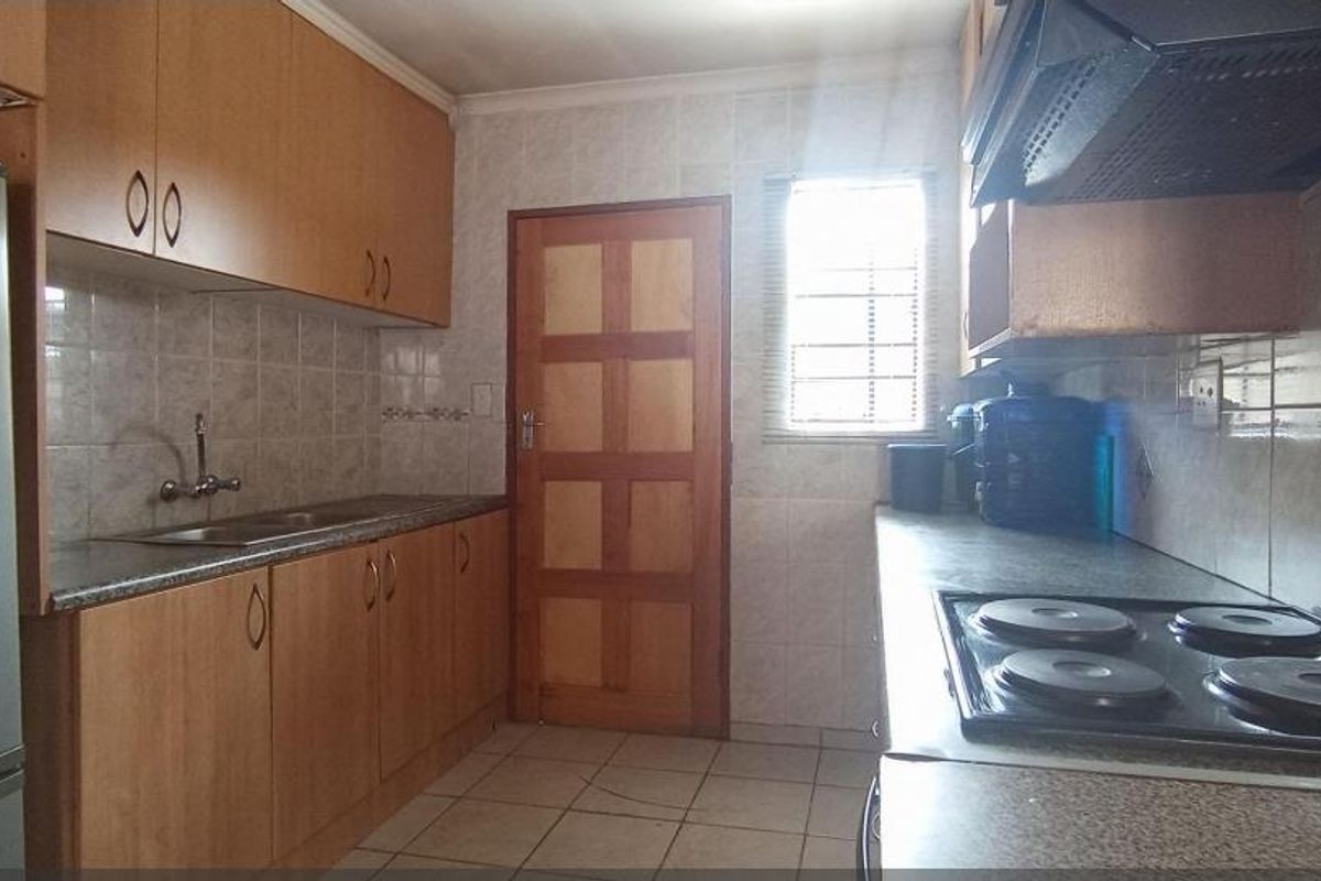 A functional kitchen featuring wooden cabinetry, tiled splashbacks, a built-in hob, and an extractor fan, with direct access to an exterior door.