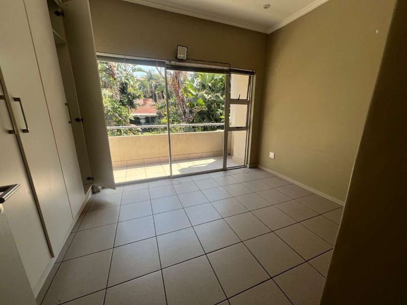 An empty bedroom featuring tiled flooring, built-in cupboards, and a sliding glass door providing direct access to a private balcony.