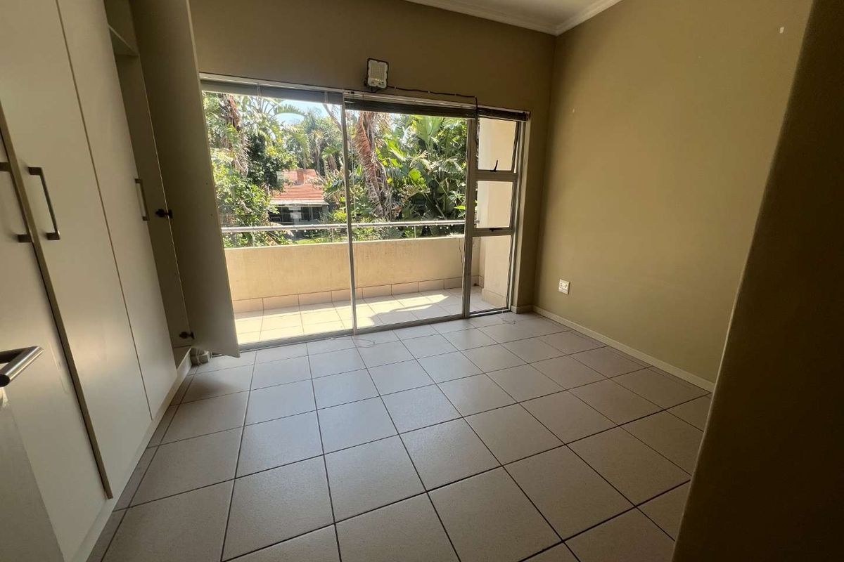 An empty bedroom featuring tiled flooring, built-in cupboards, and a sliding glass door providing direct access to a private balcony.