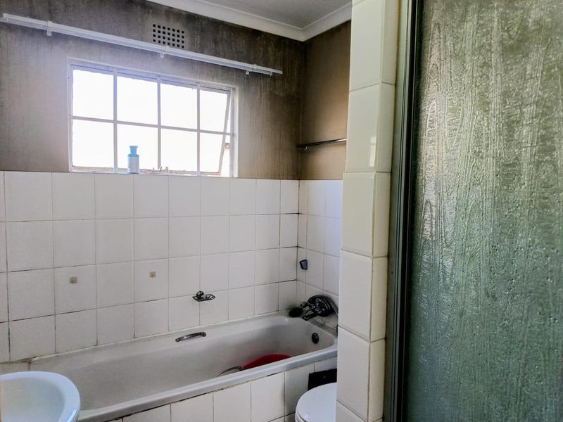 A dated bathroom featuring a bathtub and shower enclosure, requiring cosmetic updates and repairs to wall finishes and tiling.