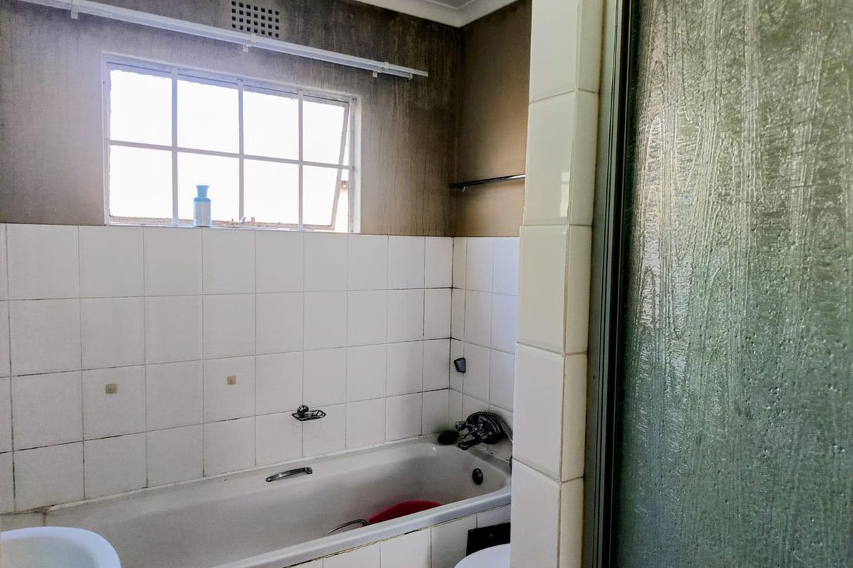 A dated bathroom featuring a bathtub and shower enclosure, requiring cosmetic updates and repairs to wall finishes and tiling.