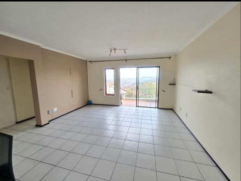 An empty, open-plan living area featuring tiled flooring, neutral walls, and a sliding glass door that opens to a balcony with scenic views.