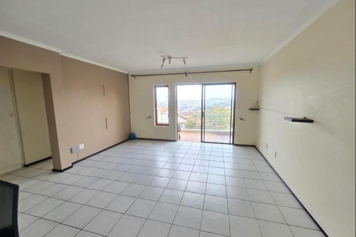 An empty, open-plan living area featuring tiled flooring, neutral walls, and a sliding glass door that opens to a balcony with scenic views.
