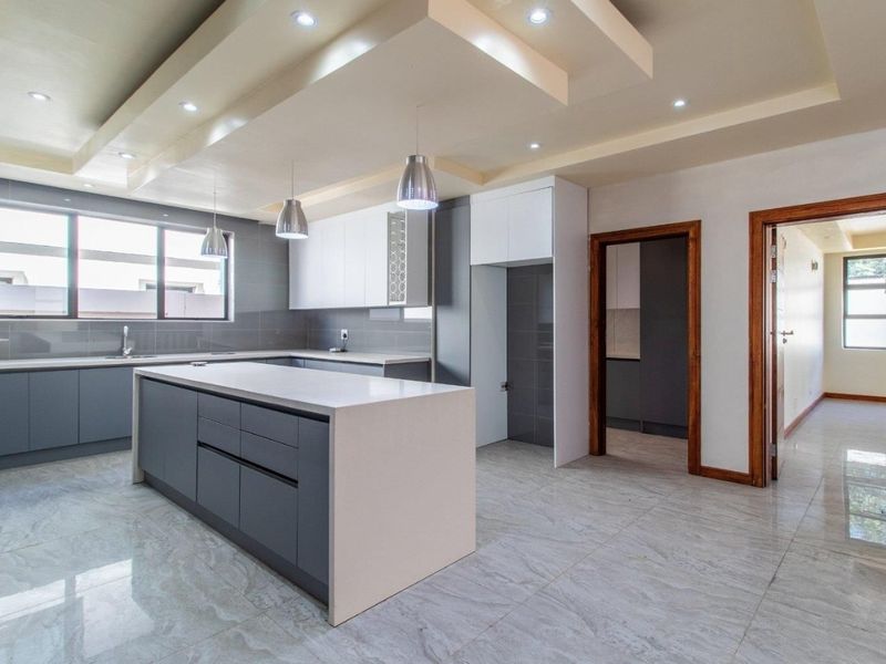 Modern kitchen featuring a large central island, quartz countertops, sleek cabinetry, and recessed ceiling lighting with a contemporary bulkhead design.