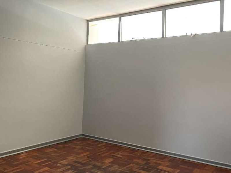 An empty bedroom featuring original parquet flooring, neutral walls, and high-level clerestory windows providing natural light.