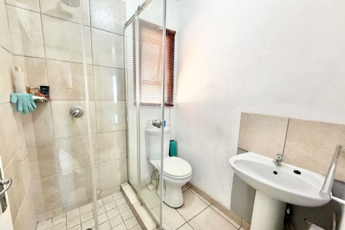 A functional bathroom featuring a glass-enclosed shower, pedestal basin, and toilet with neutral wall and floor tiling.