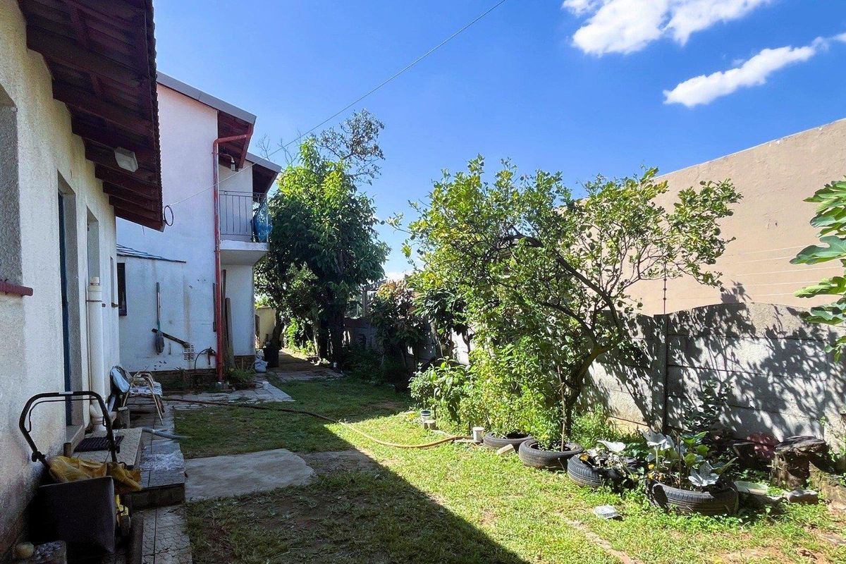 Rear exterior view of the property featuring a garden area, boundary wall, and side elevation of the house with a balcony.