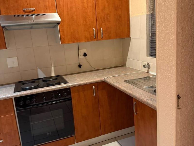 A functional kitchen featuring wood-look laminate cabinetry, built-in oven with electric hob, extractor fan, and tiled flooring.