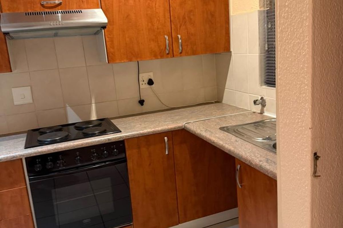 A functional kitchen featuring wood-look laminate cabinetry, built-in oven with electric hob, extractor fan, and tiled flooring.