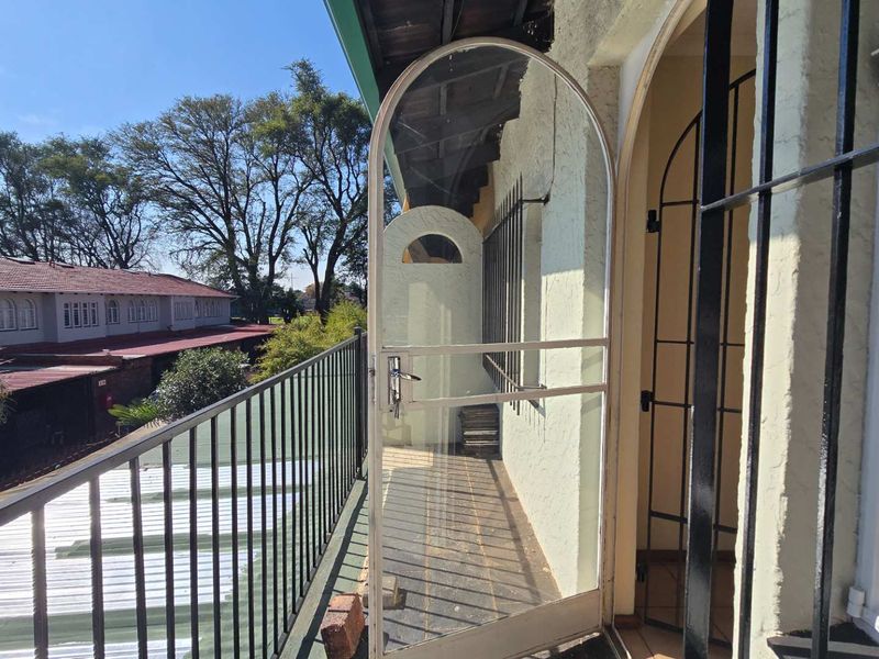 A balcony featuring a metal security gate, arched doorway, and metal balustrade, offering an outdoor space with views of the surrounding complex.