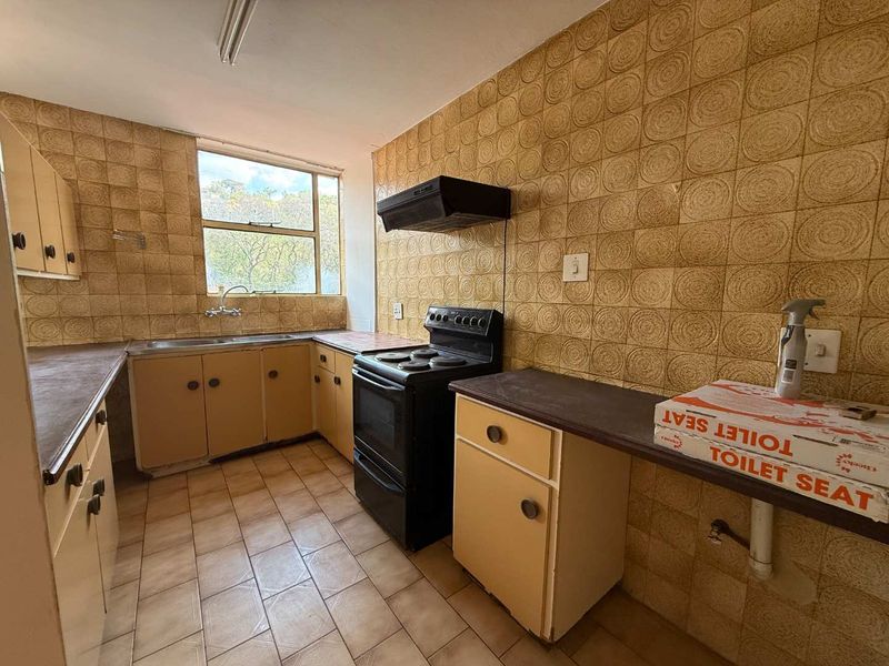 A dated kitchen featuring original cabinetry, tiled splashbacks, and a freestanding stove, offering significant potential for a modern renovation.