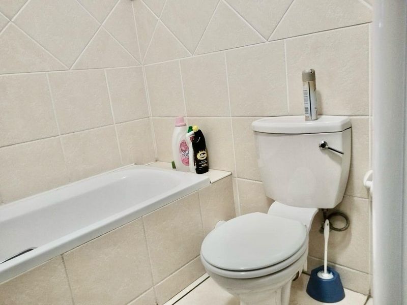 A functional bathroom featuring a standard bathtub and toilet with neutral ceramic wall tiling.