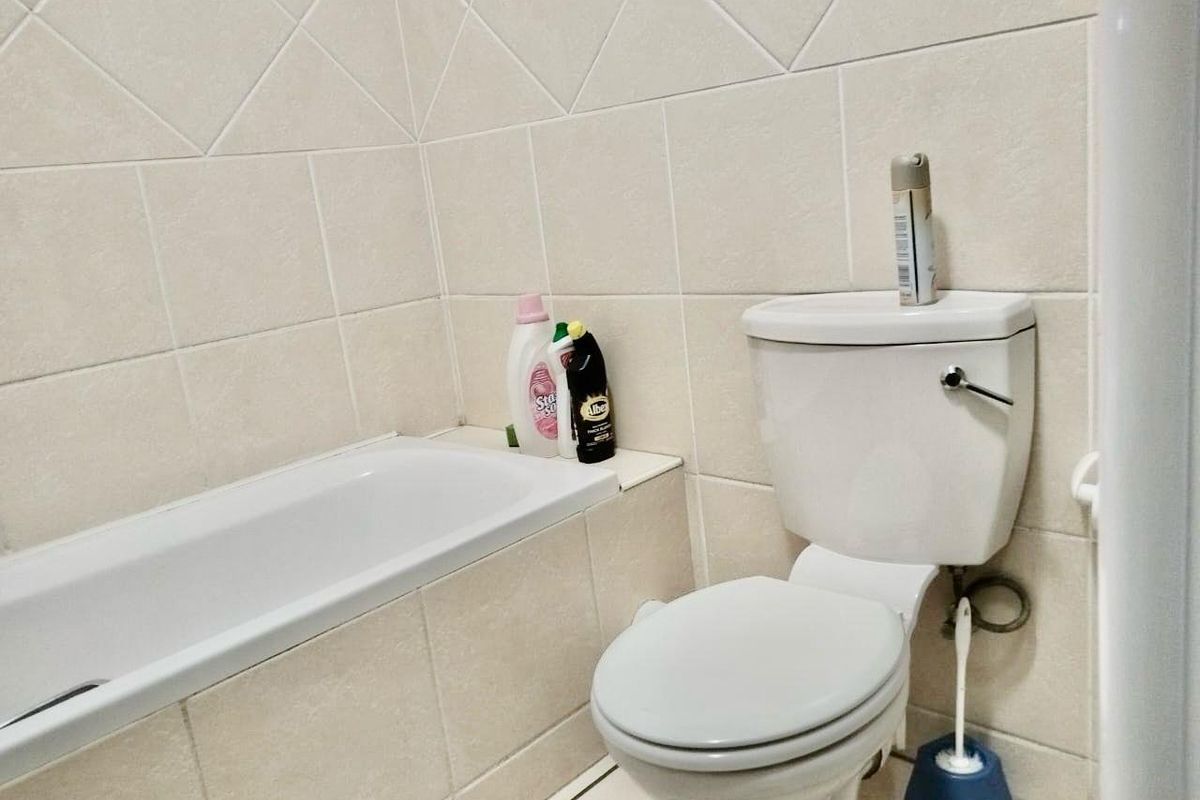 A functional bathroom featuring a standard bathtub and toilet with neutral ceramic wall tiling.