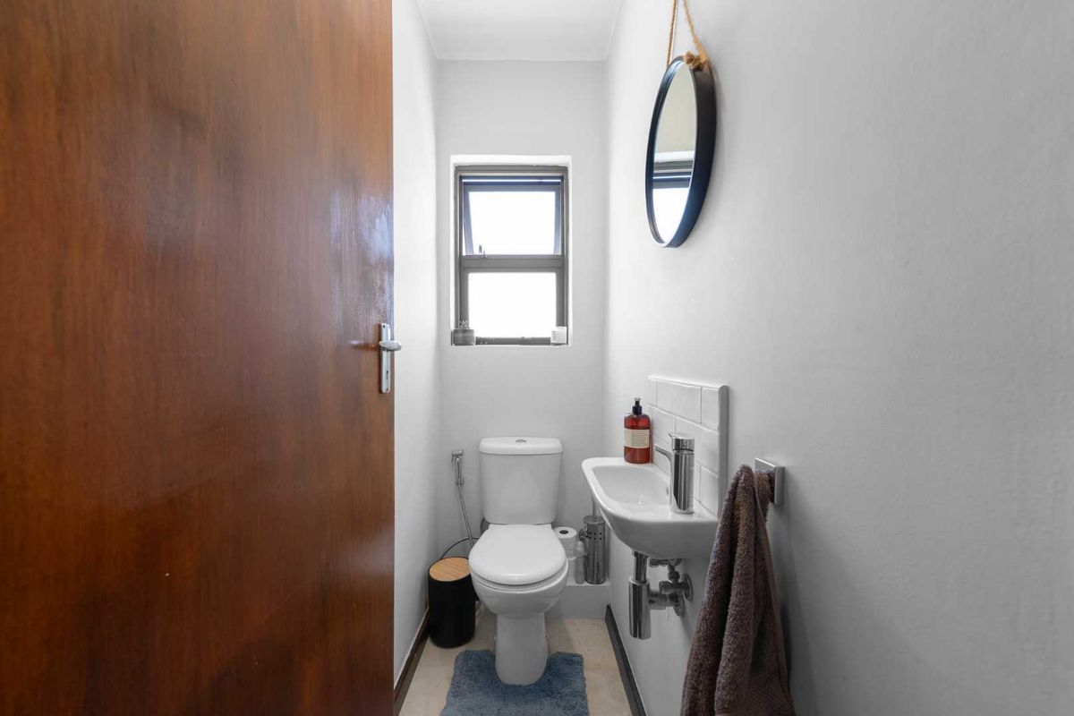 A compact guest bathroom featuring a wall-mounted basin with chrome faucet, tiled splashback, and a standard toilet.