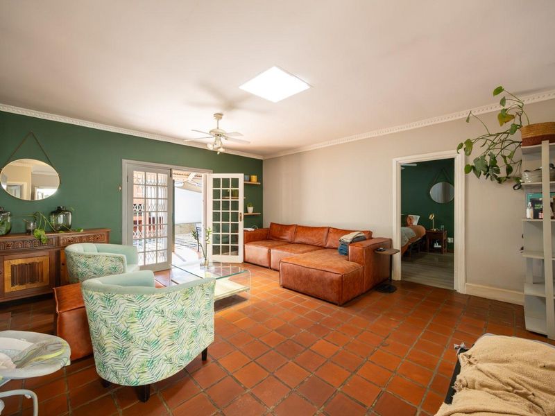 Spacious living room featuring terracotta tile flooring, a central ceiling fan, a skylight, and double french doors providing access to the outdoor area.