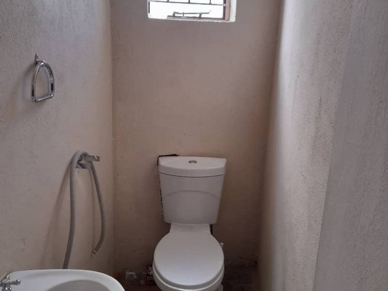 A compact bathroom featuring a standard toilet, pedestal basin, and security bars on the window, requiring cosmetic updates to finishes.