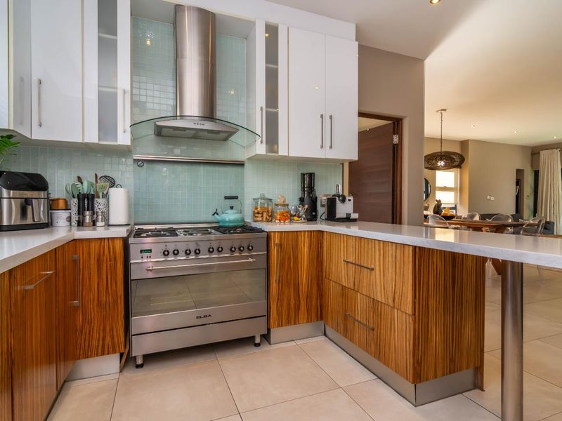 Modern kitchen featuring wood-grain and white cabinetry, quartz countertops, a stainless steel gas stove with extractor fan, and a breakfast bar.