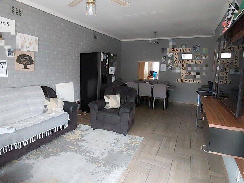 Open-plan living and dining area featuring tiled flooring, an exposed brick feature wall, and a convenient pass-through window connecting to the kitchen.