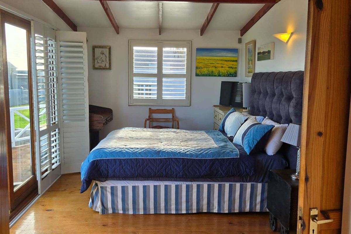 A cozy bedroom featuring exposed timber ceiling beams, polished wooden flooring, and plantation shutters, with direct access to an outdoor patio area.