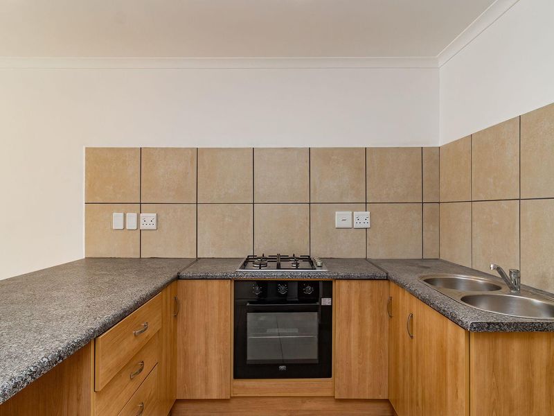 A clean, functional kitchen featuring wooden cabinetry, granite countertops, a gas hob, built-in oven, and a double stainless steel sink with tiled backsplash.