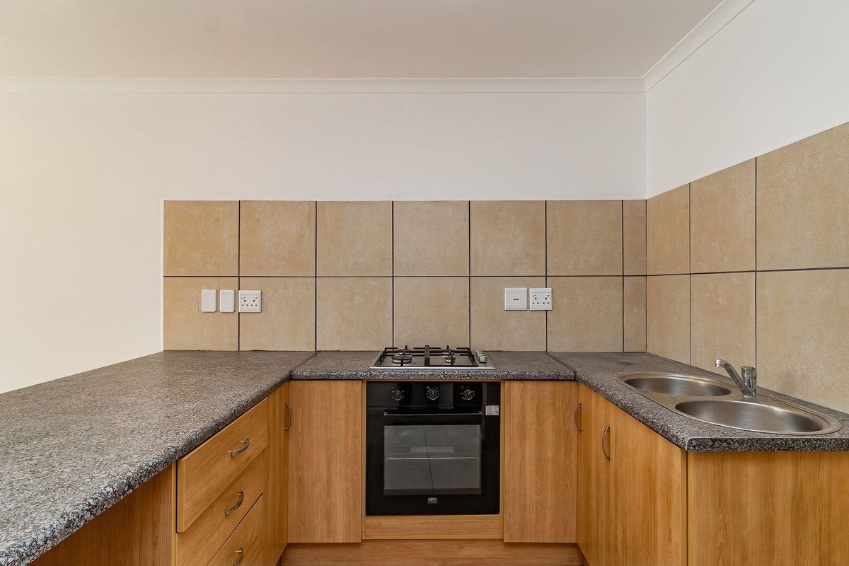 A clean, functional kitchen featuring wooden cabinetry, granite countertops, a gas hob, built-in oven, and a double stainless steel sink with tiled backsplash.
