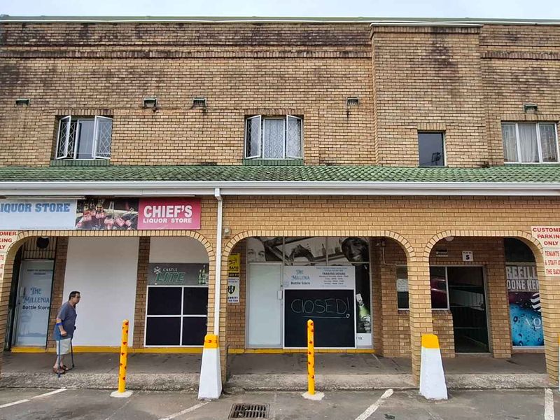 Front elevation of a commercial building featuring multiple storefronts, brick facade, and a covered walkway with parking access.
